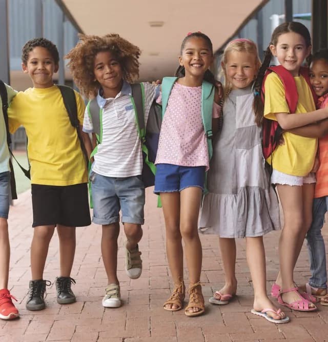 Schulkinder mit Ranzen stehen Arm in Arm nebeneinander